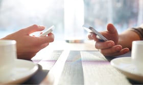 Två händer med mobiltelefoner på ett köksbord